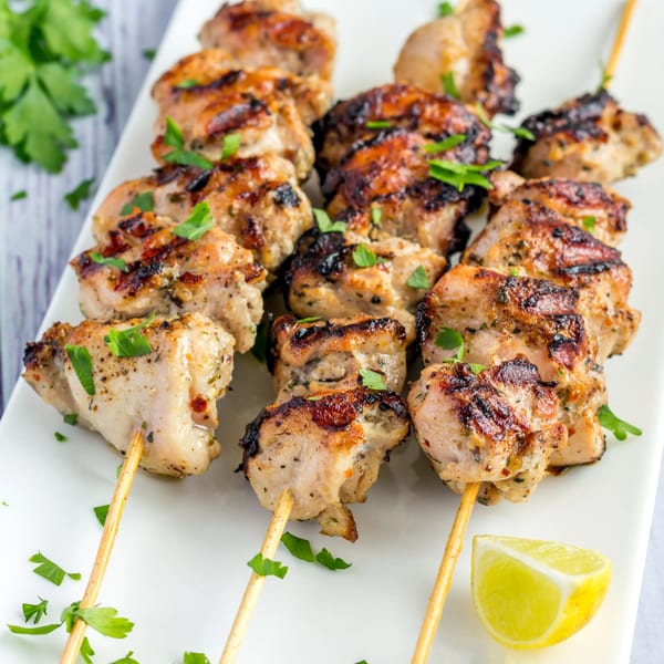 Grilled chicken kebabs with parsley and a lemon wedge on a white plate.