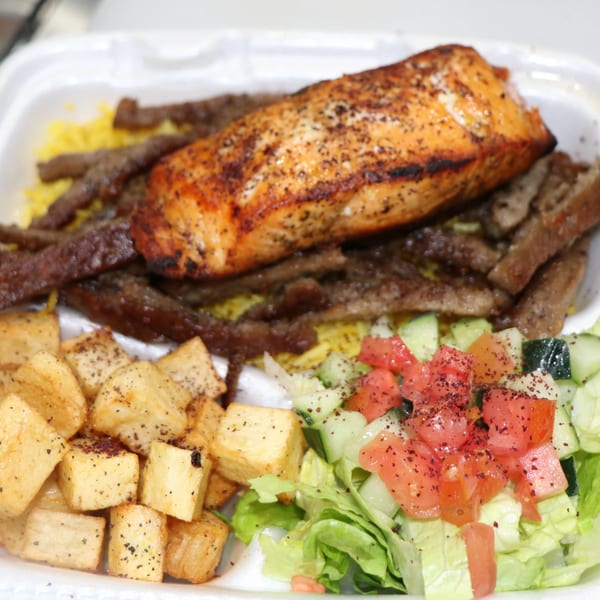 Mediterranean salmon and beef kebab plate with yellow rice, roasted potatoes, and a fresh salad.